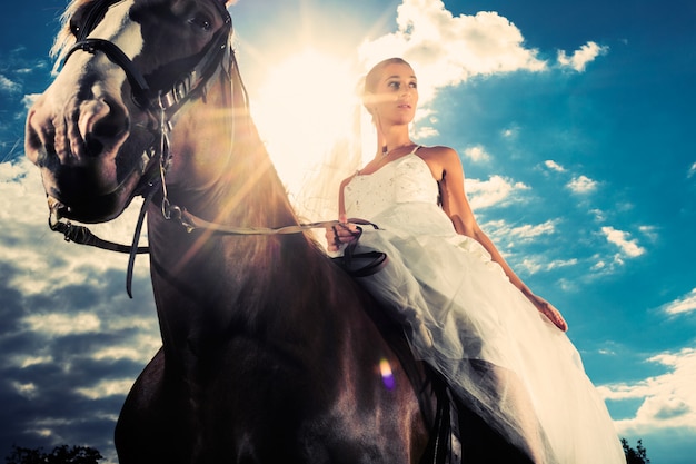 Bride in wedding dress riding a horse, backlit