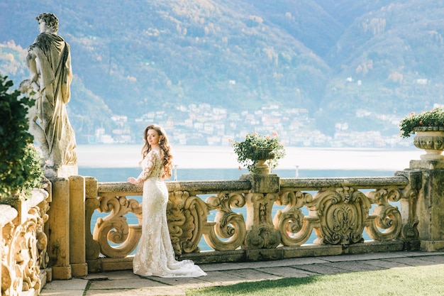 Bride in a wedding dress stands on a beautiful balcony overlooking mountains and lake