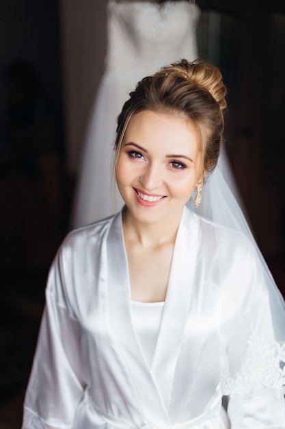 Bride in white bathrobe with make up and bridal veil crossed arm