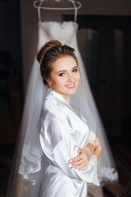 Bride in white bathrobe with make up and bridal veil crossed arm