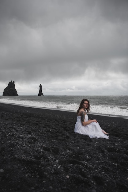 bride in white clothes stands on a black sand beach near the Atlantic Ocean in Iceland