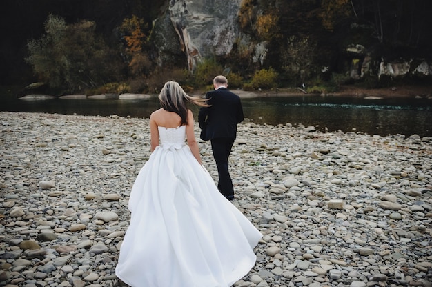 Bride in a white dress and groom go to the river stones