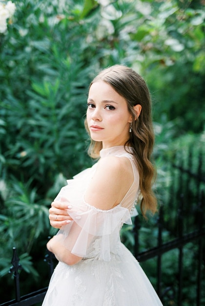 Bride in a white dress stands near a wroughtiron fence portrait