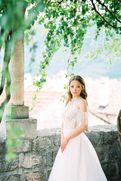 Bride in a white dress stands in a stone gazebo