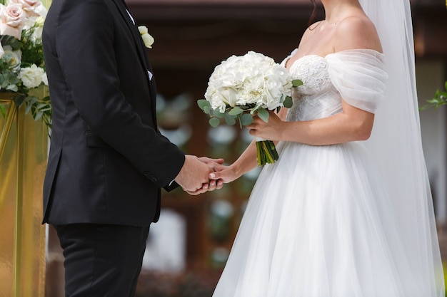 bride in white dress with beautiful bouquet of white roses and groom on wedding ceremony wedding day