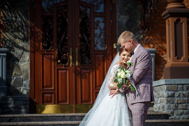 The bride in a white wedding dress and groom in a suit on the background of a brick building with large steps