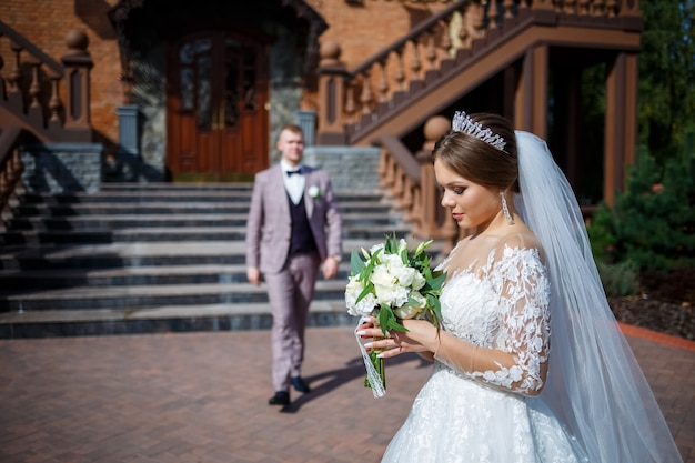 The bride in a white wedding dress and groom in a suit on the background of a brick building with large steps