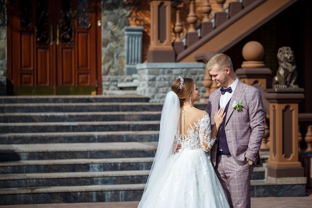 The bride in a white wedding dress and groom in a suit on the background of a brick building with large steps