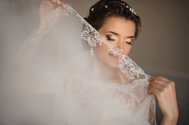 Bride with blue eyes and gentle make-up covers her lips with a veil