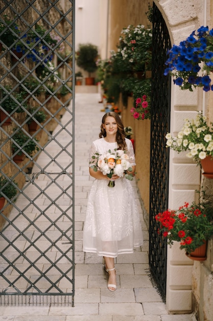 Bride with a bouquet of flowers comes out of an old courtyard with a decorative gate