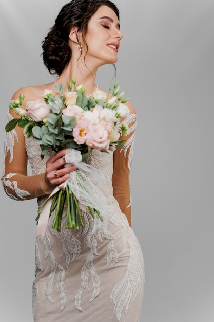 Bride with wedding bouquet looks right side. Attractive girl vertical portrait for social networks. Girl in wedding gown on blank wall.