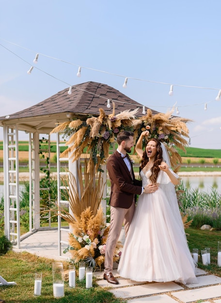 Brides celebrating engagement outdoors near decorated arch with dried flowers