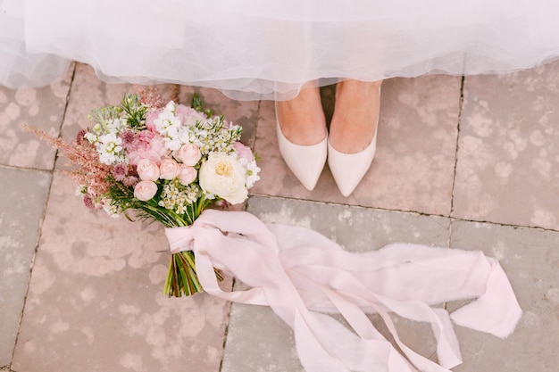 The brides legs in graceful white shoes peek out from under the skirt next to the brides bouquet