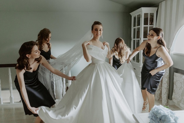 Bridesmaids helping bride put on wedding dress in hotel