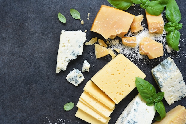 brie, blue cheese, parmesan and basil on a black concrete table.