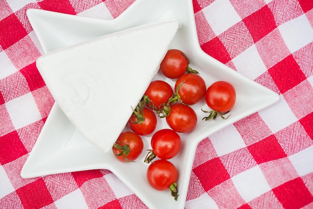 Brie cheese and cherry tomatoes on red tablecloth close up