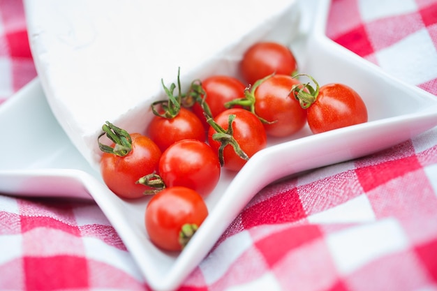 Brie cheese and cherry tomatoes on red tablecloth close up