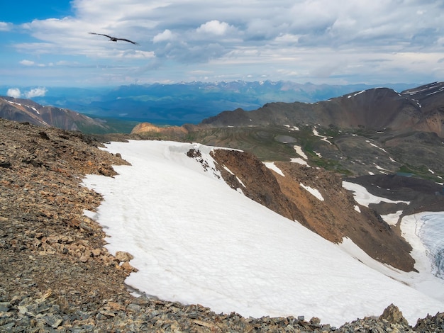 Bright alpine scenery with glacier mountains under blue cloudy sky Scenic mountain landscape in sunny weather Beautiful atmospheric view from stone hill with snow to snowy mountain range