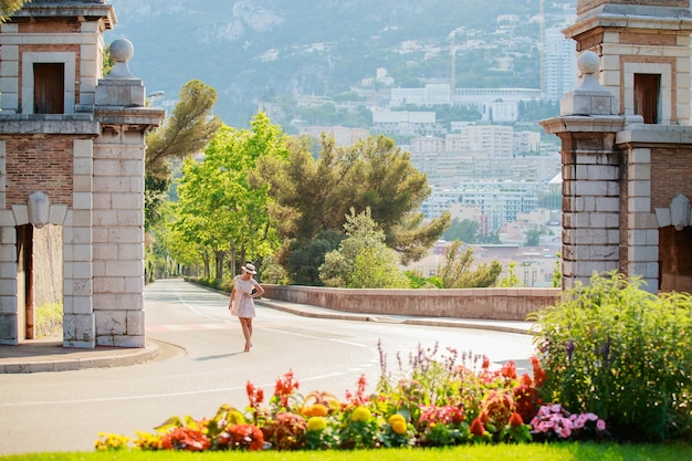 A bright beautiful girl in a light dress and hat walks along the streets of monaco in sunny weather