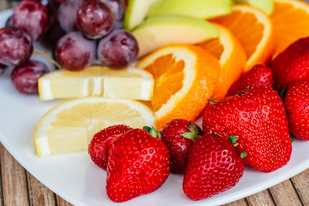 Bright berries and fruits of rainbow colors on plate - strawberry, lemon, orange, apple, grapes