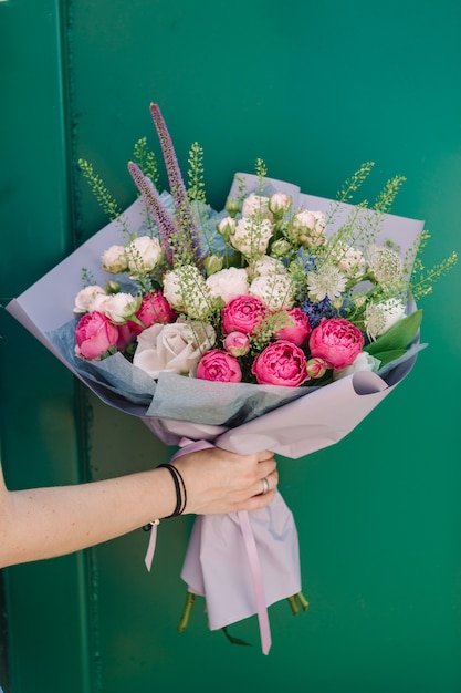 Bright bouquet of roses in hand on a green surface