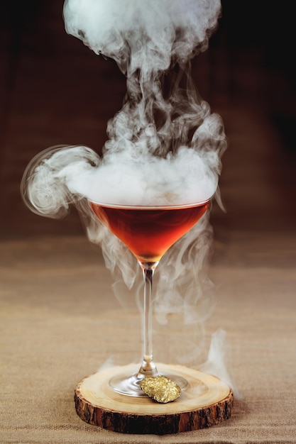 A bright cocktail with enveloping smoke on a wooden stand. Cooling alcoholic beverage.