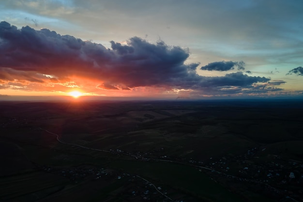 Bright colorful sunset sky with setting sun and vibrant clouds over dark landscape