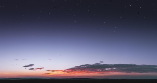 A bright colorful sunset with small saturated clouds against the background of the starry sky. Stars shine through the atmosphere at sunset