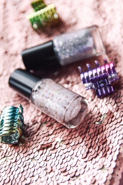 Bright composition of fashion accessories. Nail polishes and hair pins on glitter sequins surface.