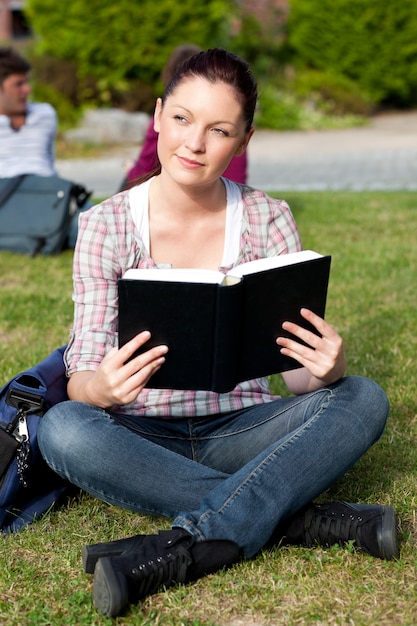 Bright female student reading a book sitting on the grass