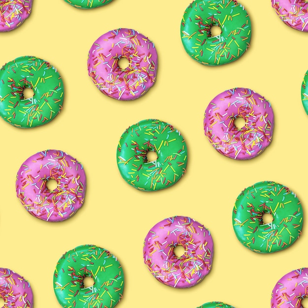 Bright flat seamless pattern with donuts. Pink and green glazed donuts with colorful sugar sprinkles on yellow background. Top view