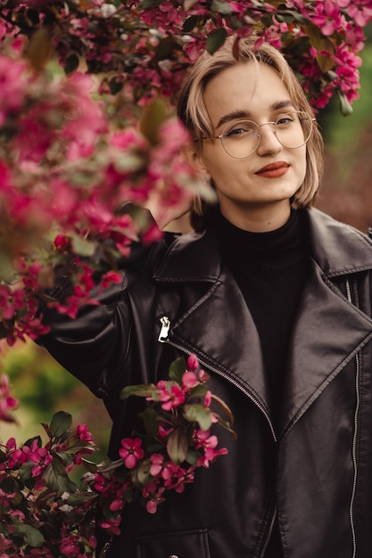 Bright fresh portrait of a young happy blonde girl in black on backdrop of pink flower tree in autum