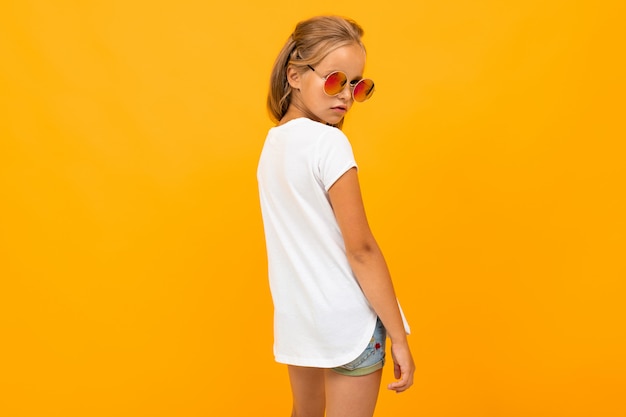 bright girl in sunglasses in a white t-shirt  stands back on a yellow wall