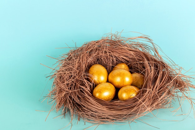 Bright golden Easter eggs in a straw nest on a blue background.