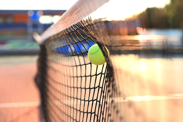 Bright greenish yellow tennis ball hitting the net.