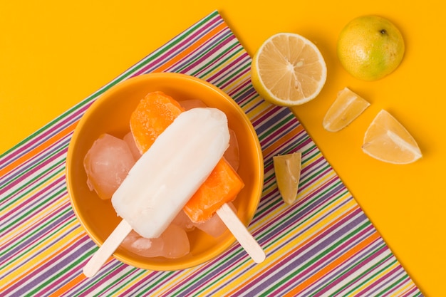 Bright ice lolly in bowl near napkin and fresh fruits