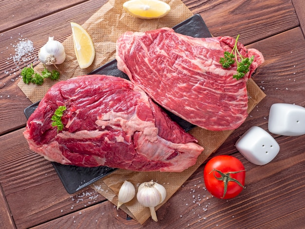 Bright juicy fresh pieces of raw beef on a wooden background surrounded by vegetables and spices. Top view