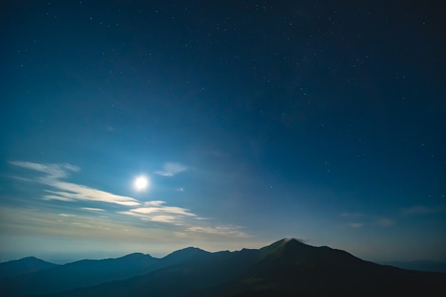 The bright moon in a starry sky above mountains