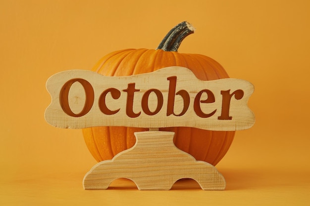 Photo a bright orange pumpkin rests prominently accompanied by a wooden sign proudly announcing october evoking autumns charm