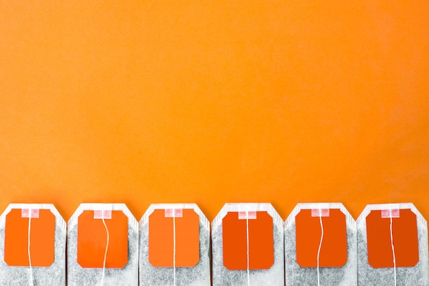 Bright orange tea bags line with herbal organic tea inside on orange background