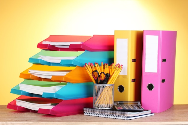 Bright paper trays and stationery on wooden table on yellow background