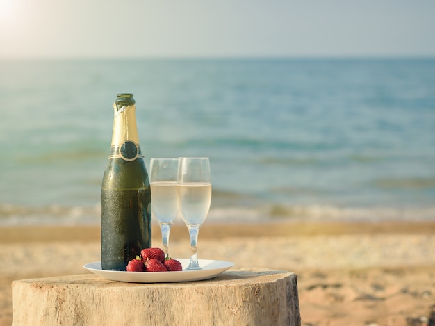 Bright rays of the sun illuminate the bottle of champagne on the beach.