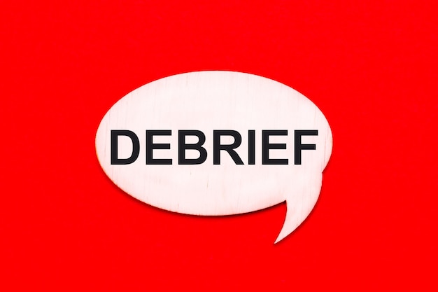 On a bright red background a light wooden curly card with the text DEBRIEF