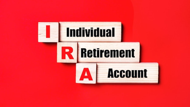 On a bright red background wooden cubes and blocks with the text IRA Individual Retirement Account Manufacturing of wooden toys