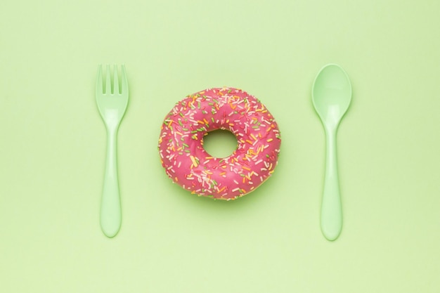 A bright red donut with a green spoon and fork on a green background The minimal concept of popular baking