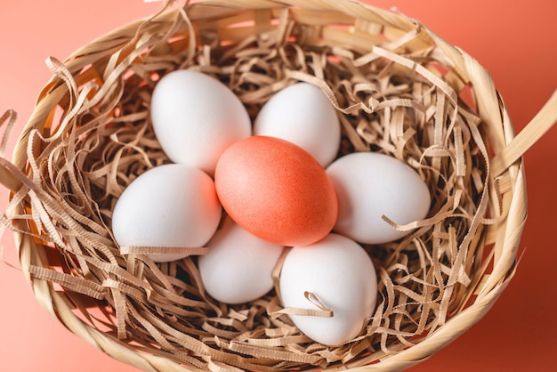 Bright red Easter egg among white ones in a basket on a light background Festive spring greeting card