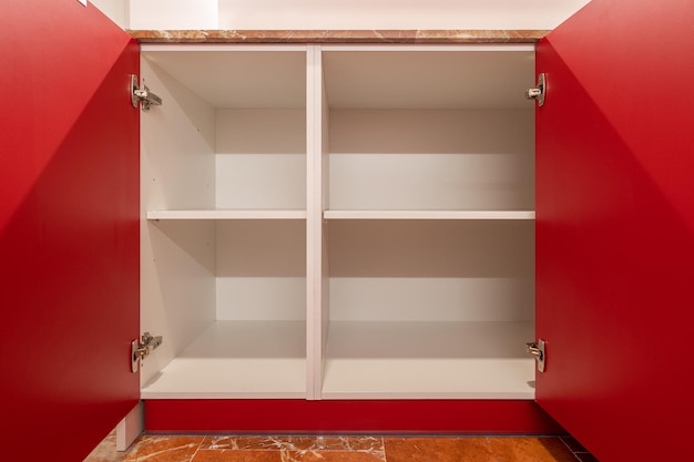 Bright red open cupboard with empty white shelves and a terracotta tiled floor