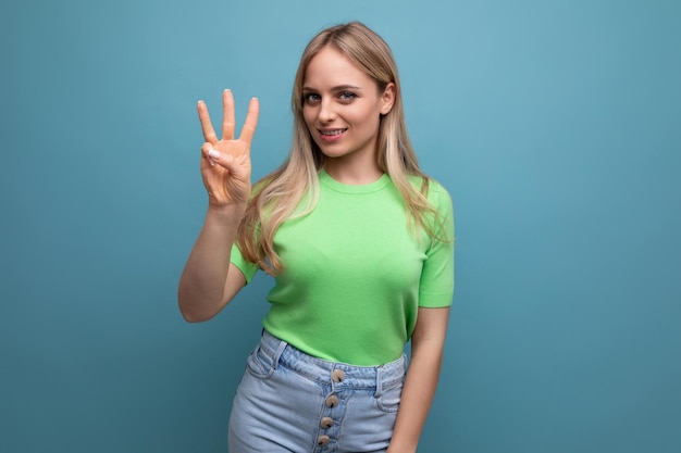 Bright smiling girl in casual outfit shows three fingers on a blue background