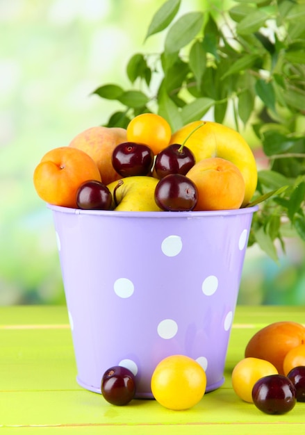 Bright summer fruits in pail on wooden table on natural background