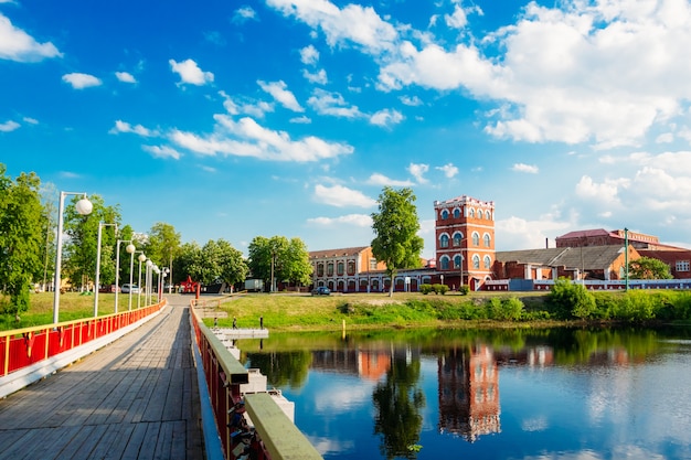 A bright summer landscape with a bridge on the river and an old factory on the shore